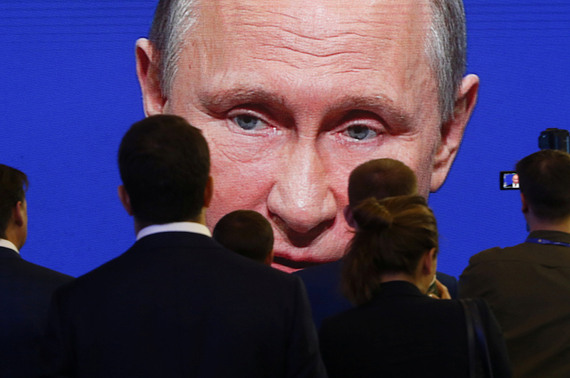 FILE PHOTO: Participants of the St. Petersburg International Economic Forum gather near an electronic screen showing Russian President Putin during a session of the forum in St. Petersburg